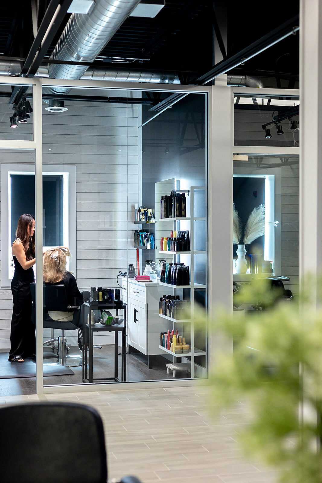 Hairdresser styling a client's hair in a modern, well-lit salon with shelves of products.