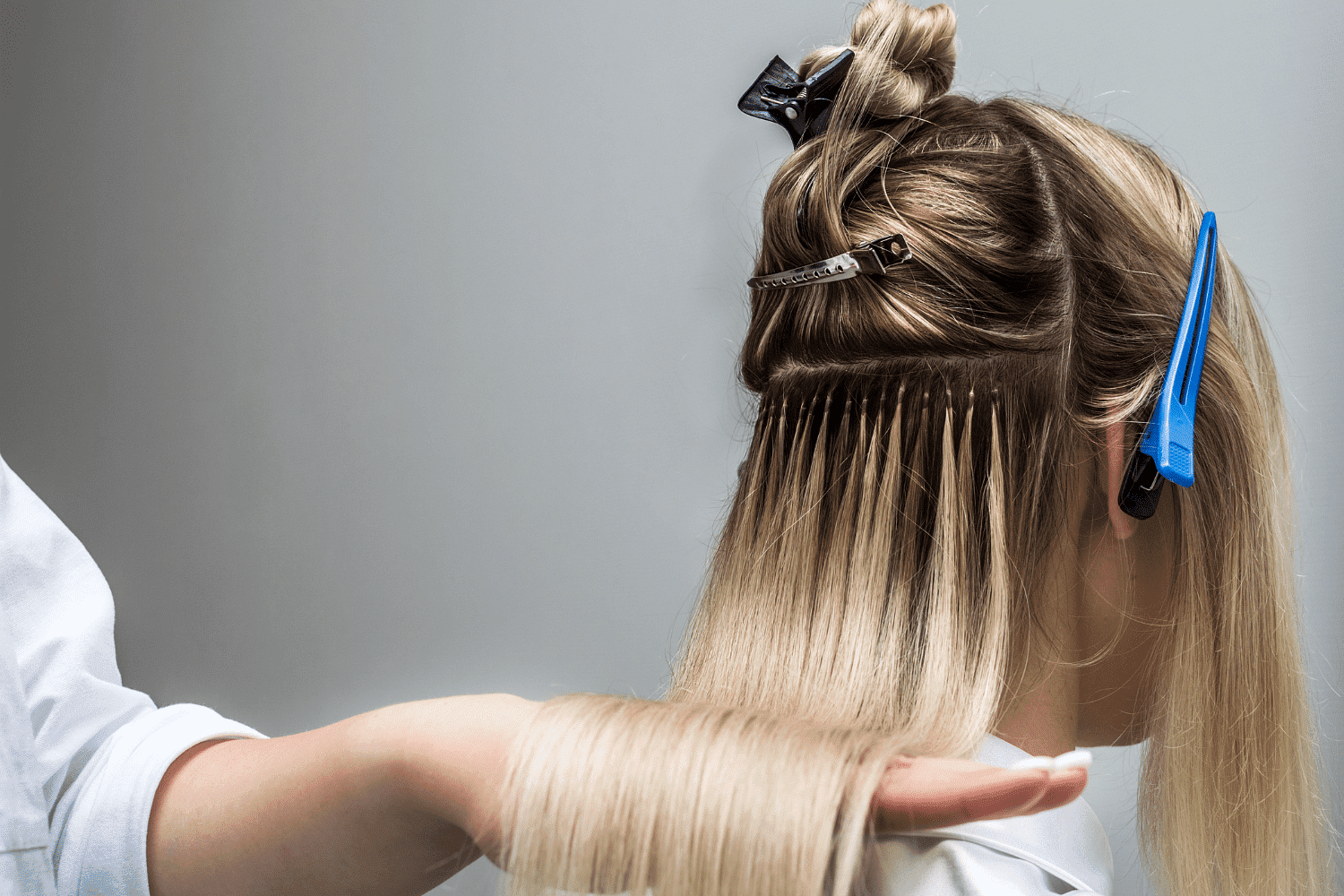 Hair extensions being applied to a blonde woman's hair in a salon.